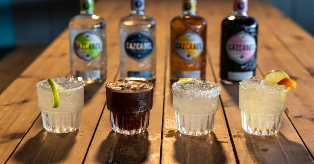 Four colorful cocktails paired with mezcal bottles on a rustic wooden table, ideal for bar settings.